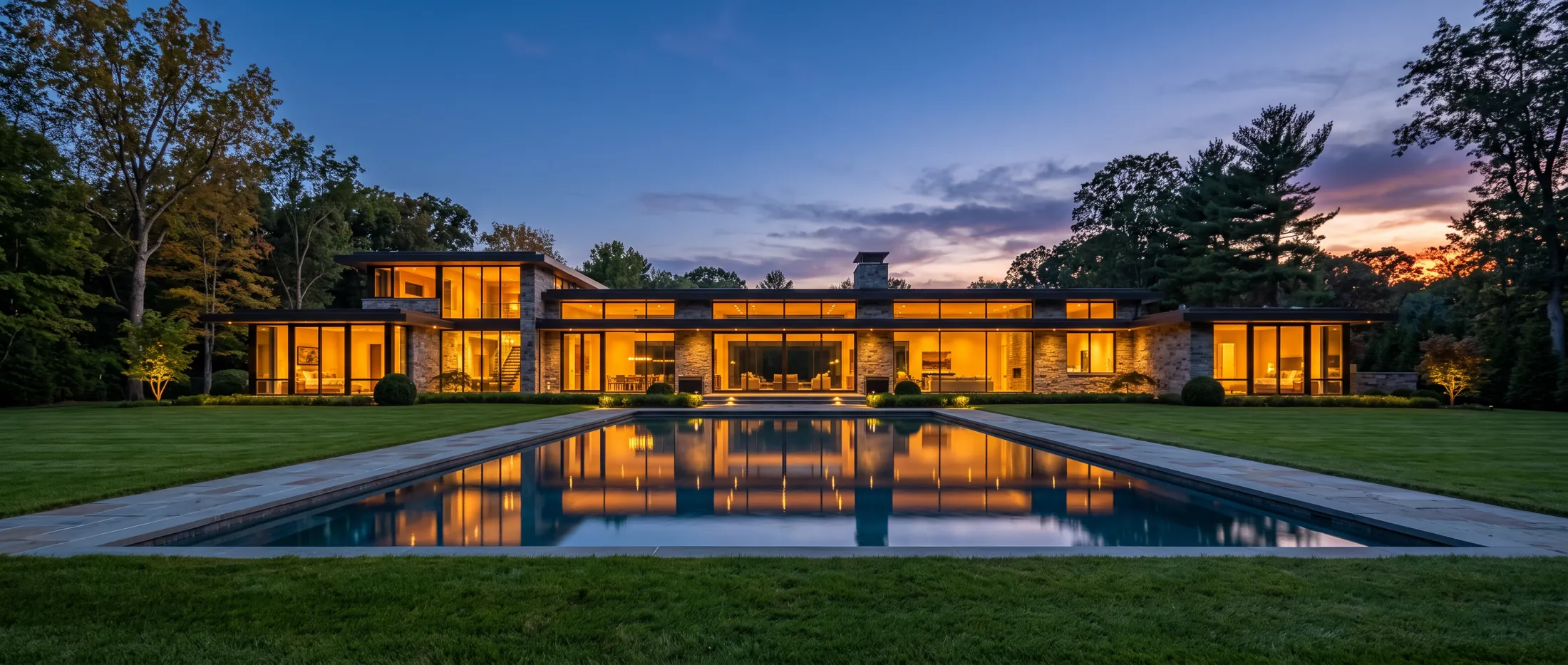 Contemporary estate glowing at dusk behind a reflecting pool
